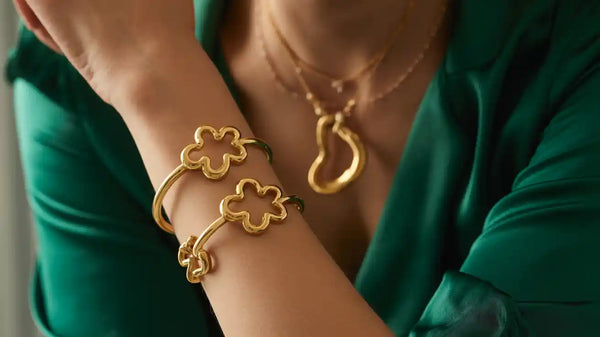 Large view of layered gold bracelets featuring clovers, chain links, and heart charm details